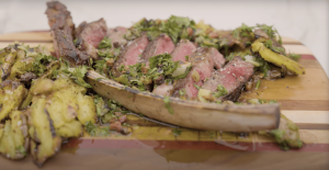 Juicy tomahawk steak off the bone with smashed potatoes and herb sauce on a wood cutting board